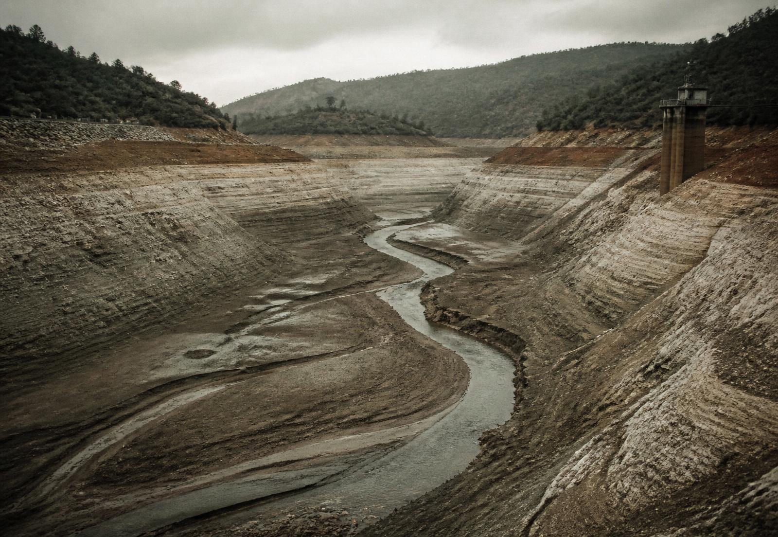 A drained reservoir with pale mineral lines marking where the water level used to be
