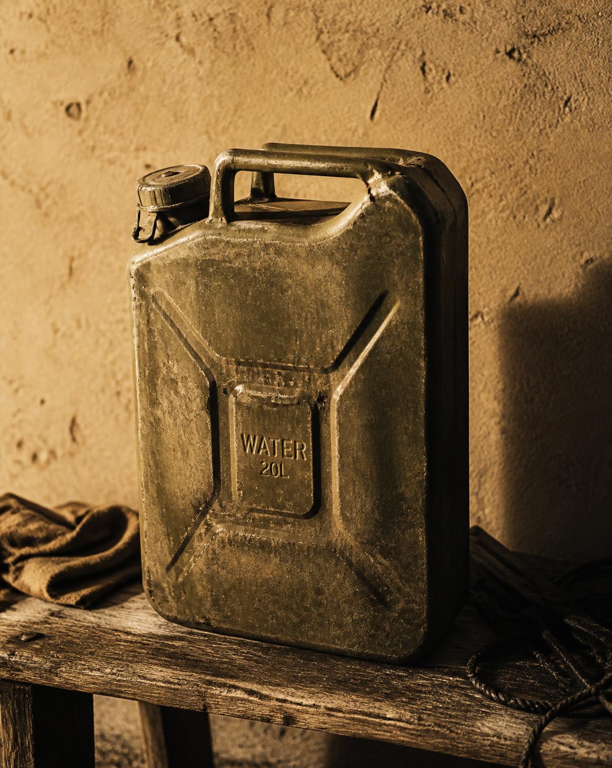A weathered steel water can stored on a rough wooden bench